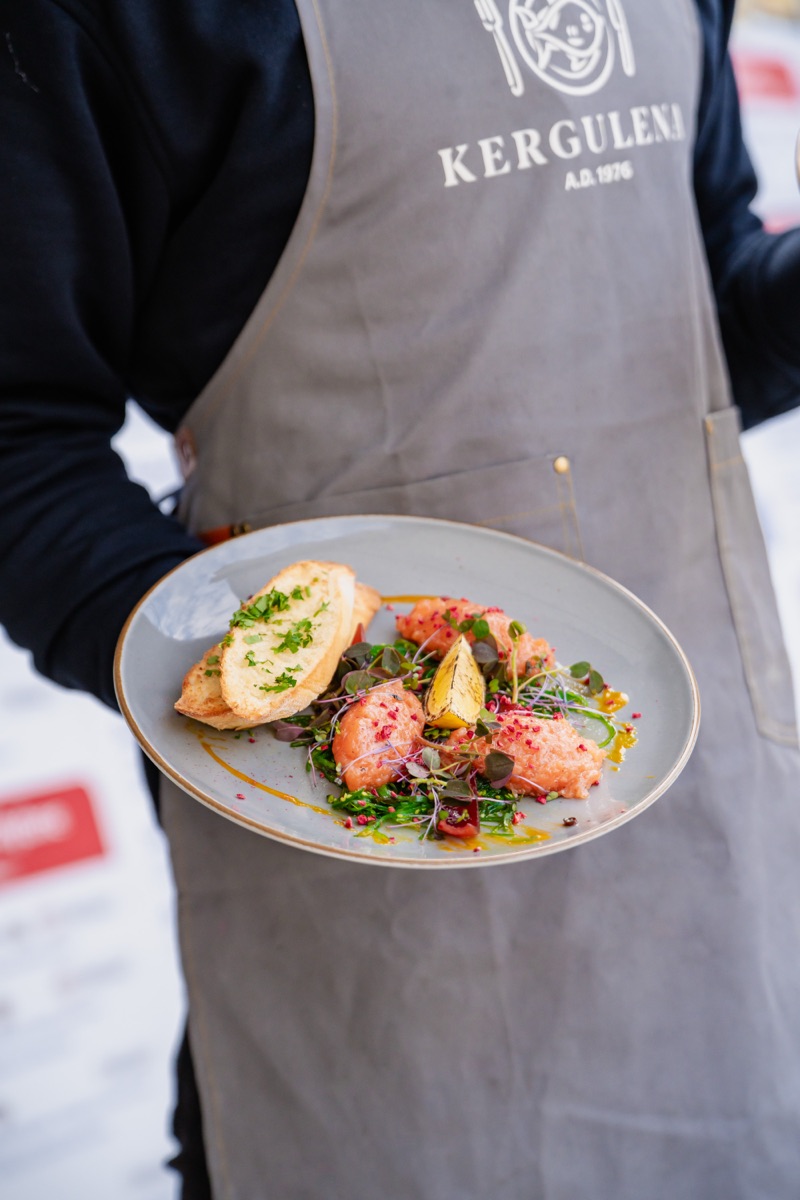 Kelner w fartuchu Kergulena A.D. 1976 serwuje talerz